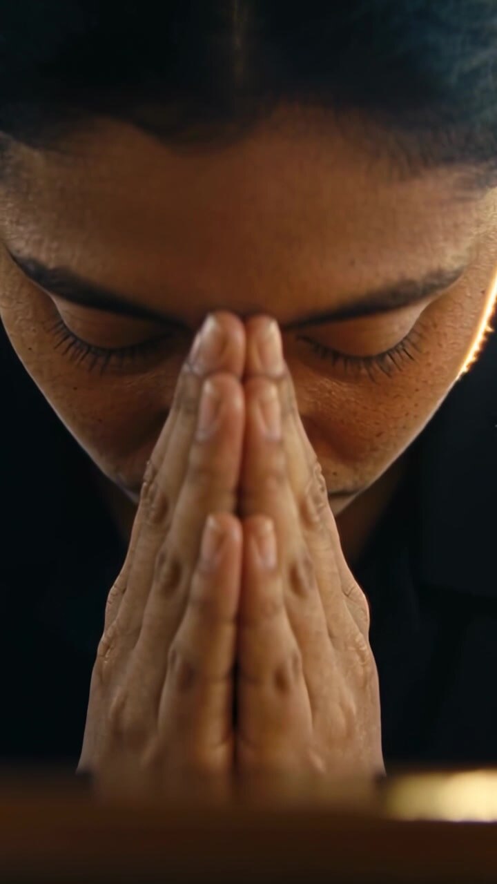 Vertical video: Filming Indian woman lowering head in dim room, praying in dark top, hands pressed