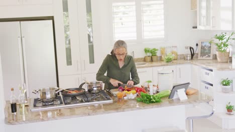 mujer mayor asiática feliz usando tableta y cocinando en la cocina