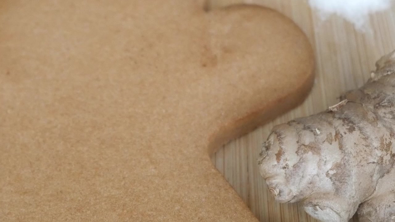Preparazione di grandi biscotti di pan di zenzero su tagliere di legno con spezie e ingredienti per la cottura nelle vicinanze, pronti per essere glassati e decorati