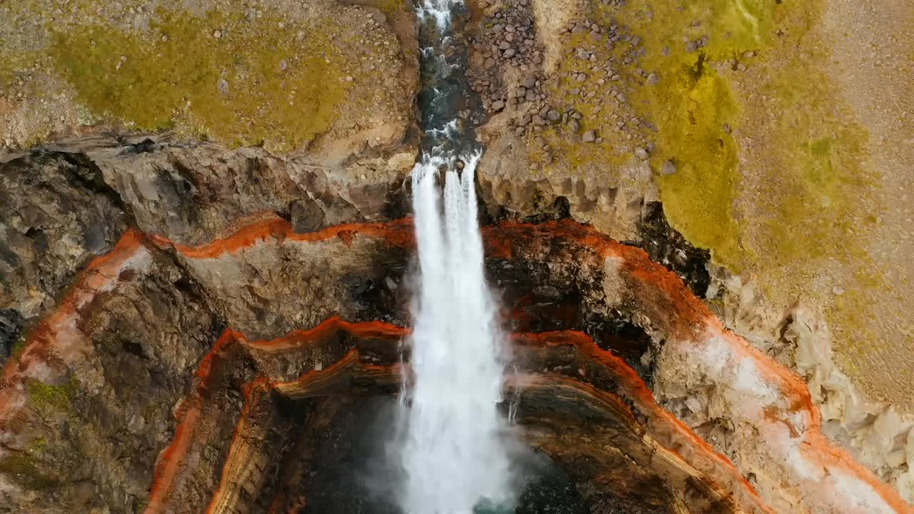 un dron 4k captura imágenes cinematográficas de un cañón con rayas de color anillo naranja en las rocas, un paisaje amarillento y una dramática cascada en el centro