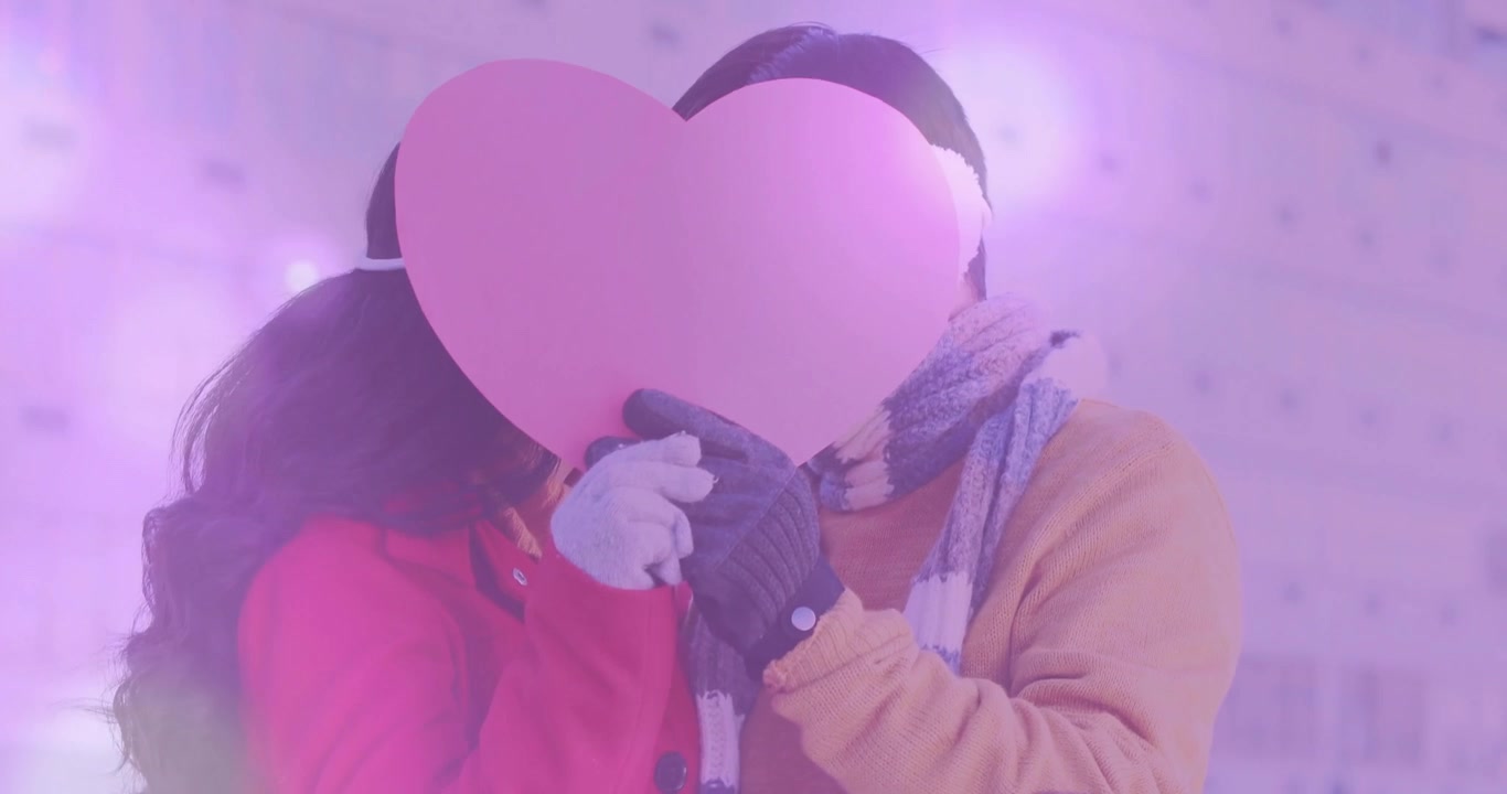 Casal entrando na varanda, segurando um adereço de coração rosa e se beijando atrás dele para marketing.