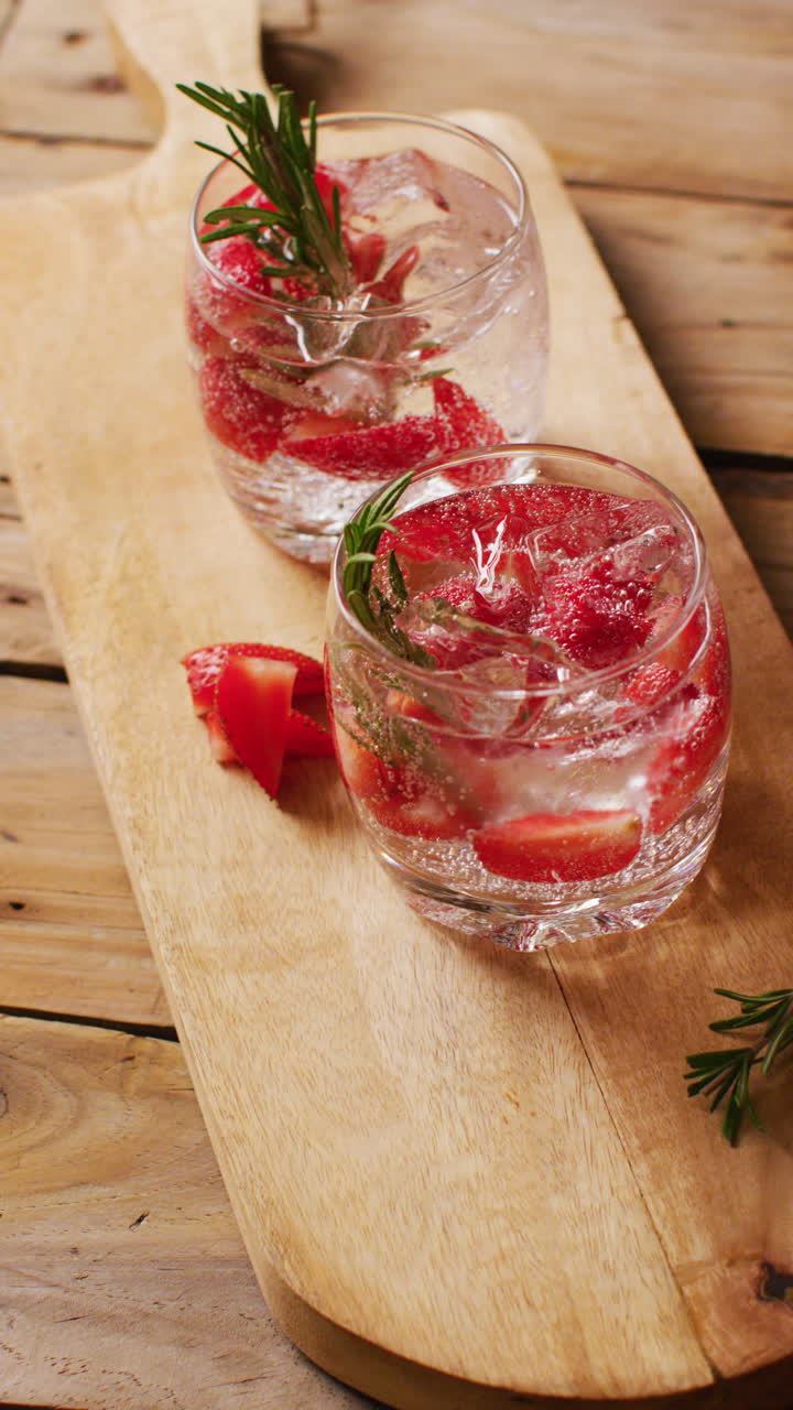 Vertical video of close up of drinks with strawberries on wooden board, with copy space