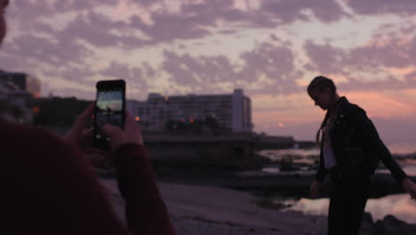 Pareja-Joven-Divirtiéndose-Tomando-Fotos-En-La-Playa-Novia-Posando-Con-Los-Brazos-Levantados-Feliz-Alegre-En-La-Playa