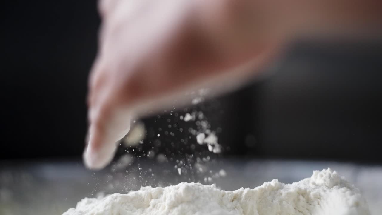Beautiful cinematic and slow motion view of a hand mixing dough and flour in a fancy kitchen, flour falling and flying in the air. Particles and specks of flour suspended in the air.