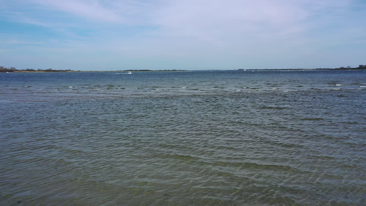 낮은 각도의 드론이 해변을 가로질러 물을 바라보며 수평선을 바라보고 있습니다.