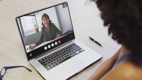 mujer afroamericana usando una computadora portátil para una llamada de video, con un colega de negocios en la pantalla