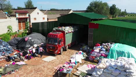 aerial shot of a truck loaded with bags, unloading old clothes and a person guiding on the ground