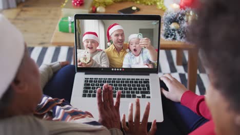 African-american-mother-and-daughter-using-laptop-for-christmas-video-call-with-family-on-screen