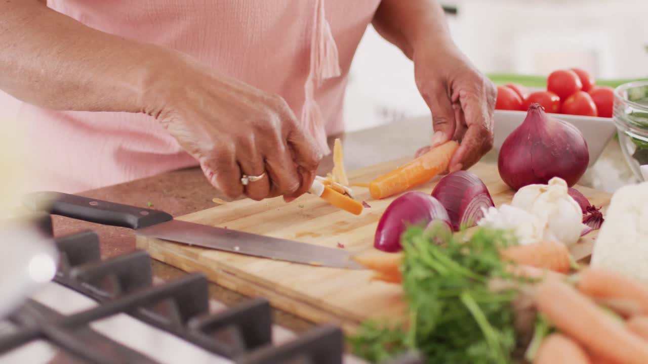 Happy senior african american woman cooking in kitchen, peeling vegetables