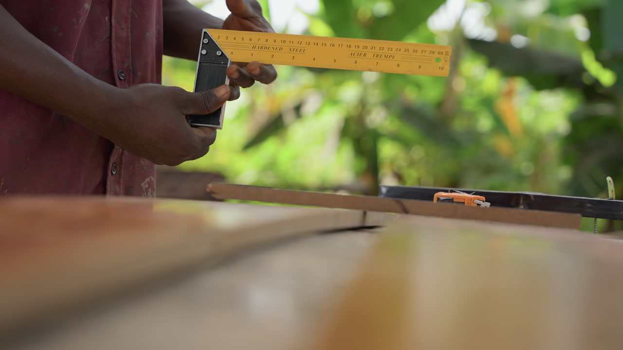 Closeup black hands aligning wooden boards outdoors with ruler and clamp, measuring spacing for deck installation, green garden backdrop, sawdust flecks, steady practical construction process, focused