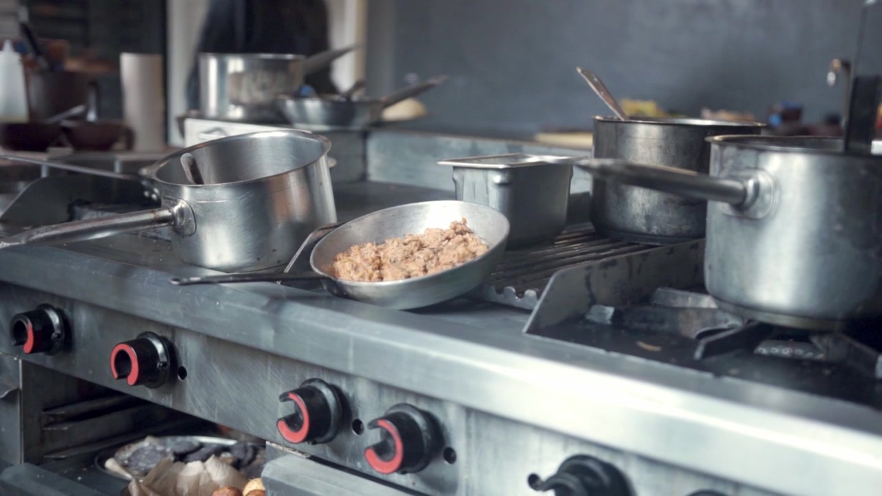 Vista ravvicinata di un fornello da cucina commerciale con pentole, tegami e ingredienti preparati durante la preparazione attiva di cibi culinari all'interno