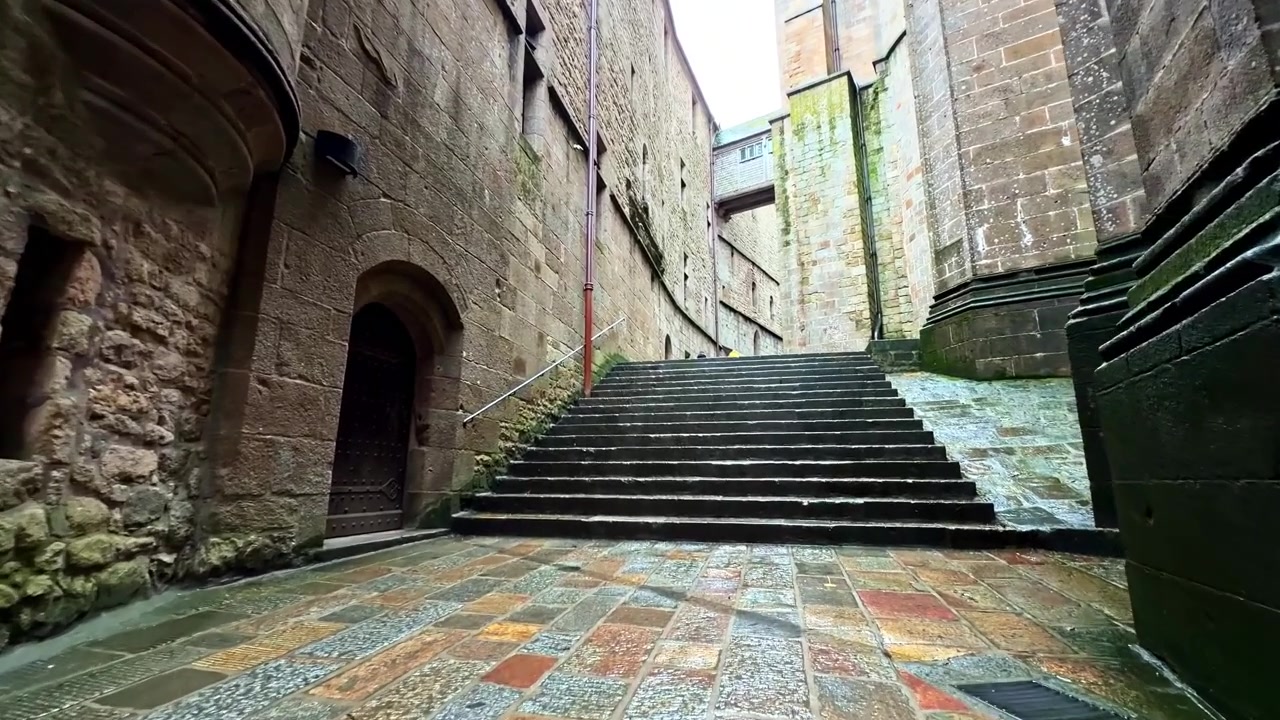 A quiet stone passageway leads through Mont-Saint-Michel with moss-covered walls. Ideal for historical or architectural content.