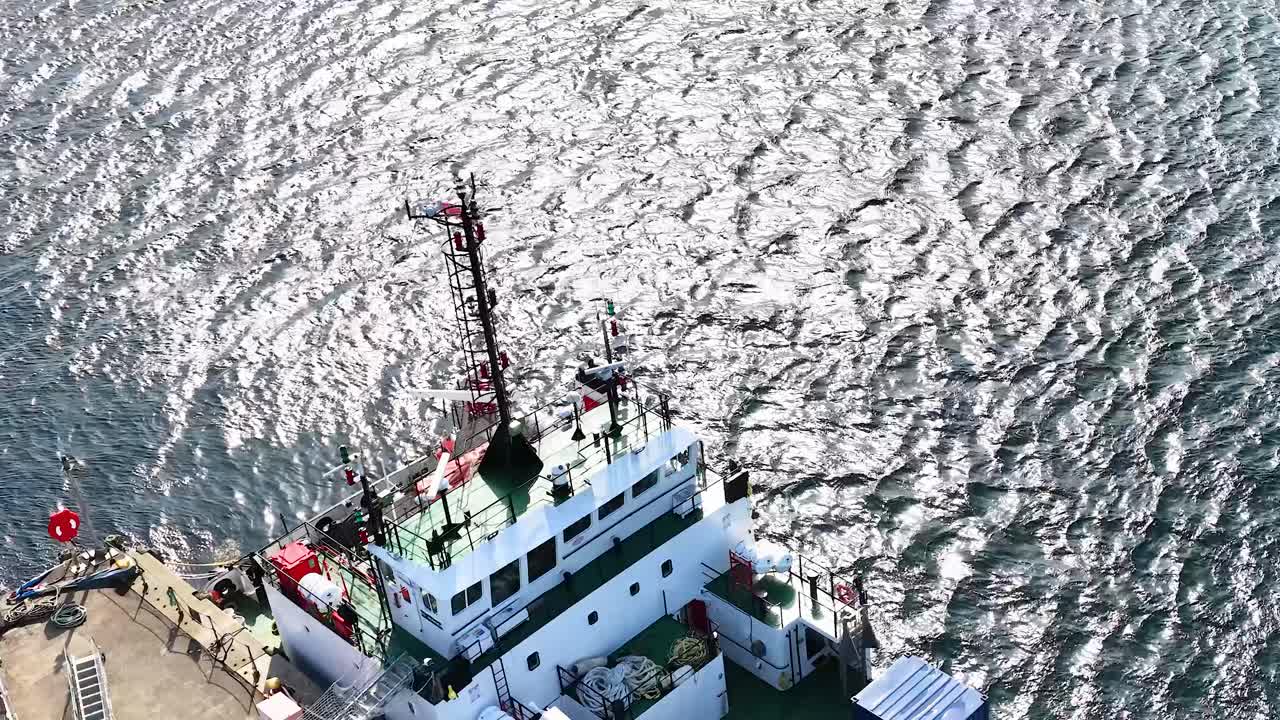 Drone aerial view circles docked vessel at Dundee pier, bright daylight, rippling water, industrial setting
