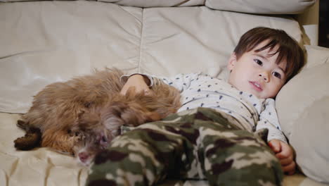 niño multiétnico fresco se relaja en el sofá con un cachorro, viendo televisión juntos