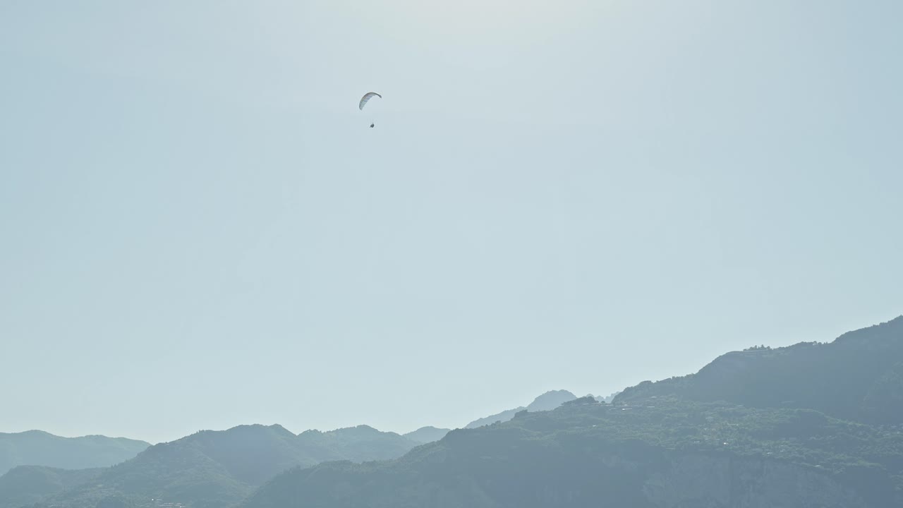 Paraglider pilot flying high above blue sunlight tinted mountains