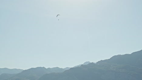 paraglider pilot flying high above blue sunlight tinted mountains