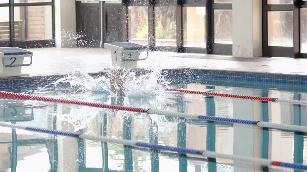 Splashing into swimming pool, swimmer diving from starting block during practice