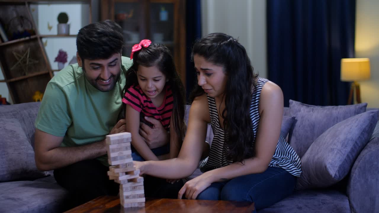 un marido y una esposa indios y su pequeña hija jugando a los bloques de construcción - crianza feliz, familia nuclear, padres jóvenes cariñosos