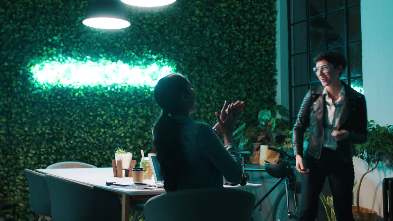 Two Women Discussing Ideas in a Modern Coworking Office at Night