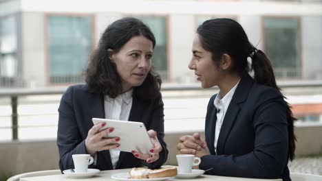 mujeres de negocios que usan tablets en un café al aire libre