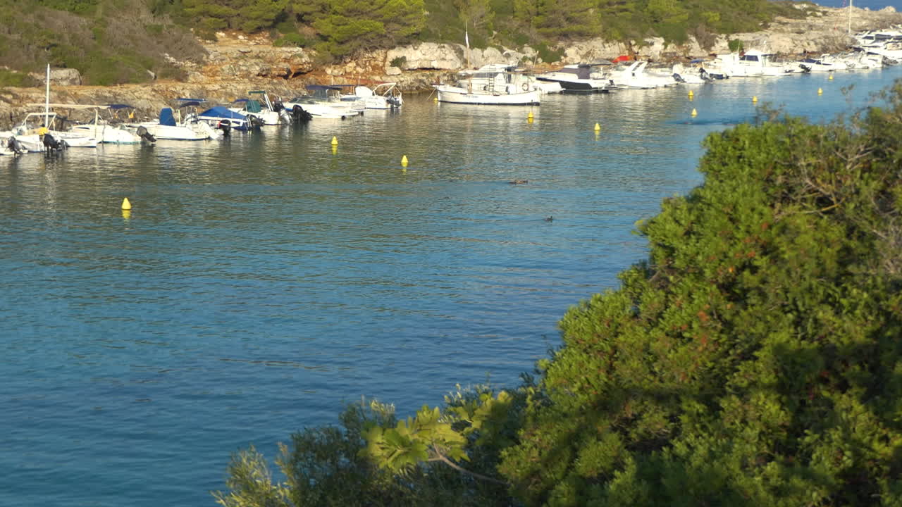 tranquila mañana soleada hora dorada vista de cala santandria en menorca con barcos, nadadores, mar azul y rocas circundantes