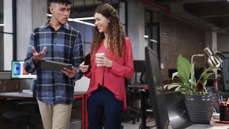 two happy diverse creative designers in discussion at tablet in casual office, slow motion