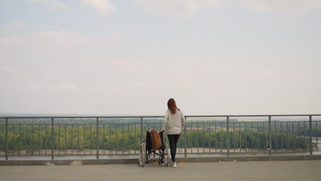 redhead woman stands by wheelchair with little girl on path