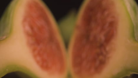 halved fresh ripe fig fruit, dolly macro close up probe lens defocused studio shot of slices of sweet soft reddish flesh containing crunchy seeds inside and green skin