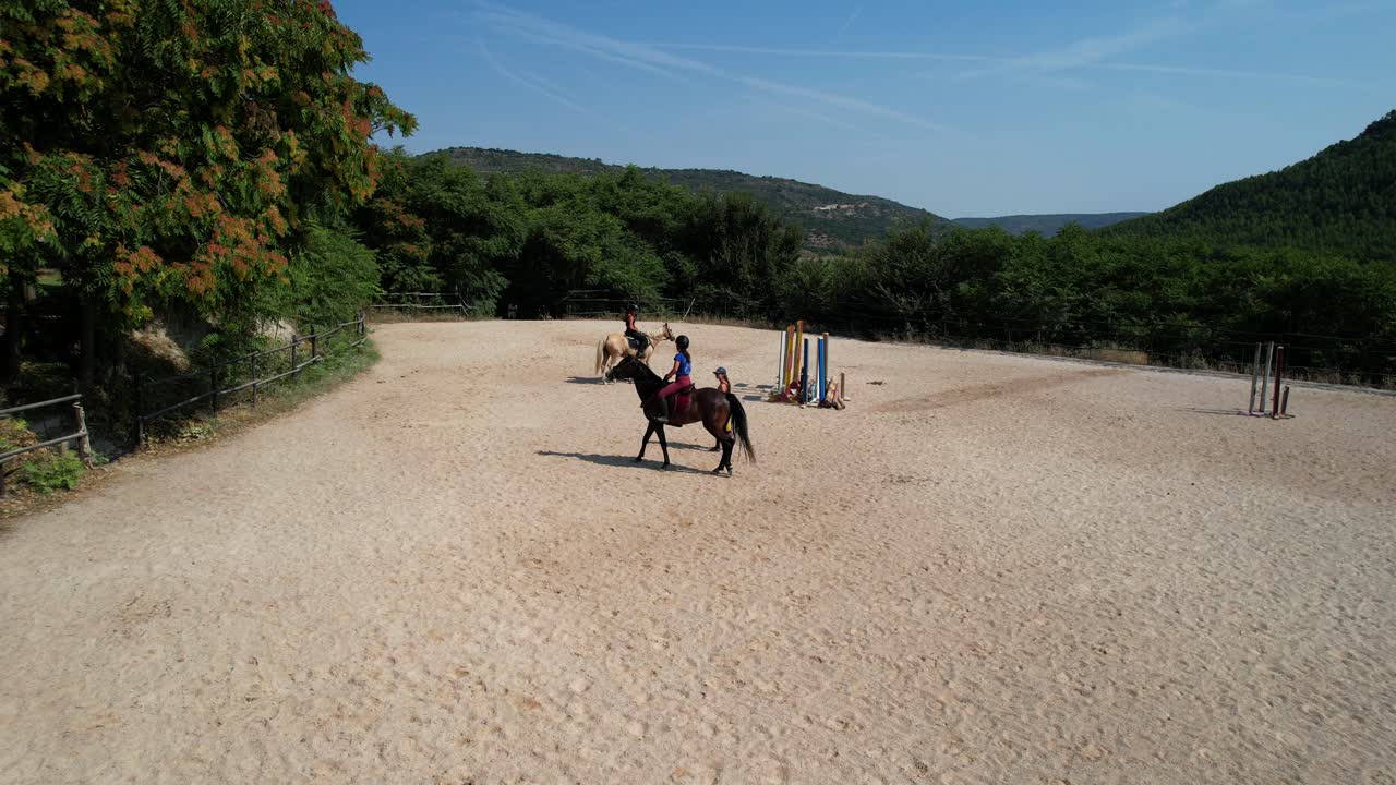 Static drone view of two riders congregating around their trainer in the arena during a lesson