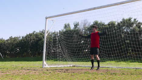 standing in front of goalpost, soccer player wearing red jersey on field