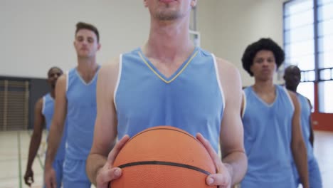 Retrato-De-Un-Jugador-De-Baloncesto-Masculino-Caucásico-Serio-Y-Un-Equipo-Masculino-Diverso-En-La-Cancha,-Cámara-Lenta