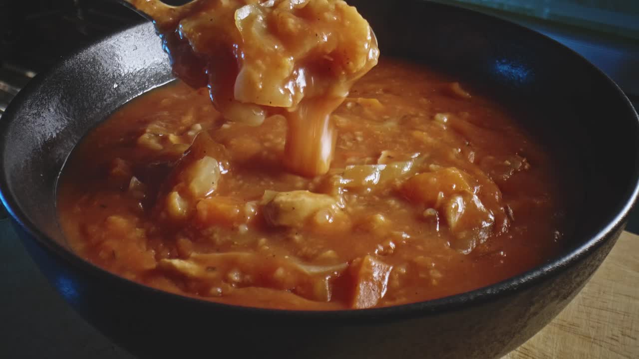 primer plano de una sabrosa sopa de estofado de verduras con trozos de pollo en un tazón con una cuchara que muestra el tamaño de la porción