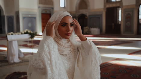 muslim bride in white dress adjusting veil in an elegant hall