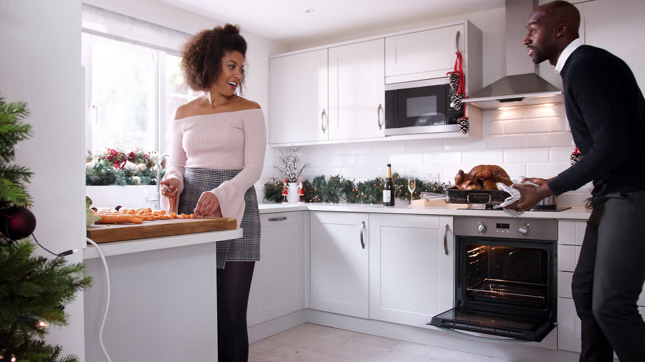 Young black couple preparing Christmas dinner together at home, man taking roast turkey out of the oven, couple basting it together, close up