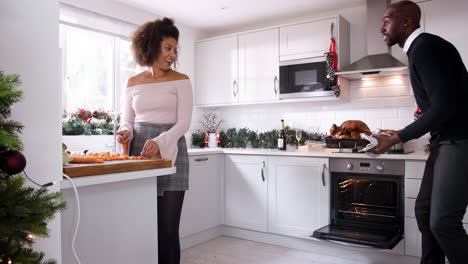 Joven-Pareja-Negra-Preparando-La-Cena-De-Navidad-Juntos-En-Casa,-Hombre-Sacando-Pavo-Asado-Del-Horno,-Pareja-Rociándolo-Juntos,-Cerca