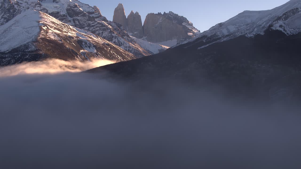 Ripresa aerea che si innalza tra le nuvole per rivelare le montagne di Torres del Paine durante l'ora d'oro.