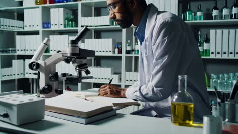 scientist writing notes in a laboratory with a microscope