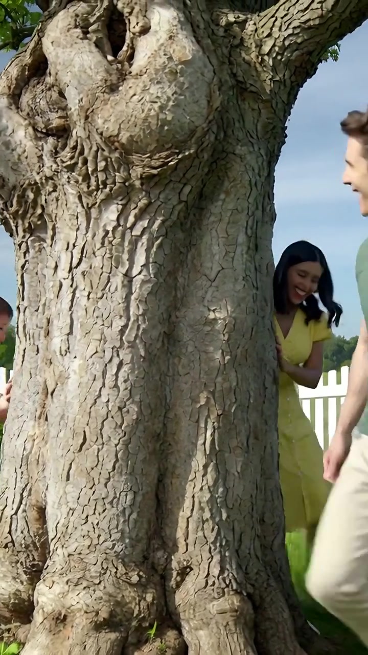Vertical video: Playing child in red shirt running past gnarled tree in yard, man in green watching