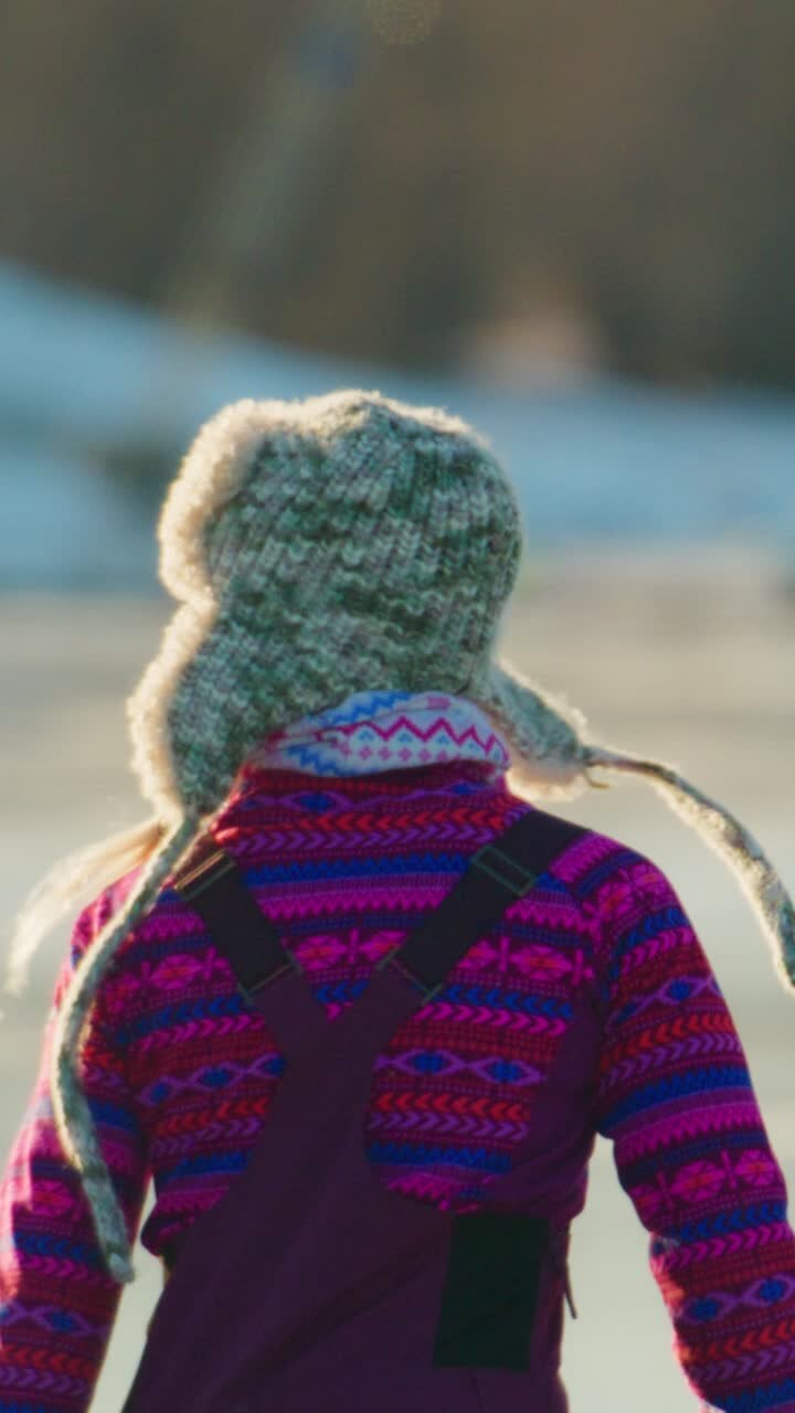Gioviale skater in vivaci abiti invernali con un cappello di pelliccia che scivola sul ghiaccio, godendosi il freddo della stagione e irradiando felicità ed energia in un paesaggio gelido