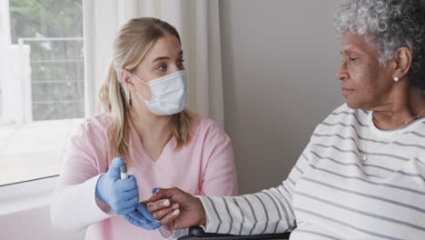 Caucasian-female-nurse-in-face-mask-checking-sugar-of-senior-african-american-woman,-slow-motion