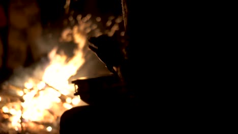 silhouette of drummer playing with hands on percussion drum by campfire