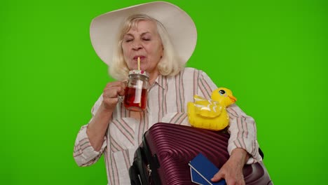 mature woman traveler tourist passenger drinking cocktail, holding passport, tickets, luggage bag