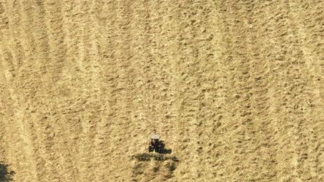 aerial view of a tractor harvesting golden crops in a large open field under sunny skies