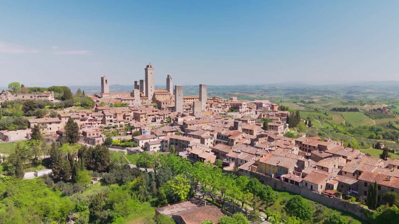 Drone stazionario che ruota la telecamera lungo la parete laterale di San Gimignano, Toscana, Italia, rivelando un tratto più lungo della città collinare, torri medievali e caldi tetti toscani.