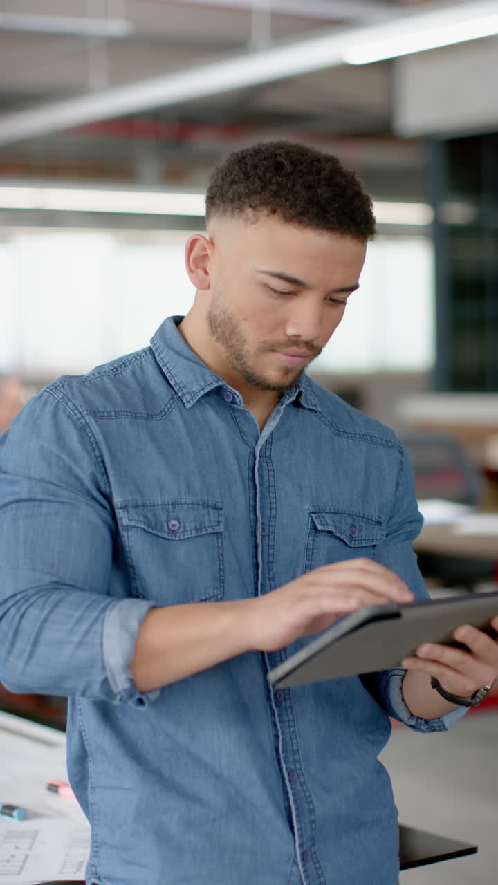Vertical video of portrait of happy biracial businessman using digital tablet at office