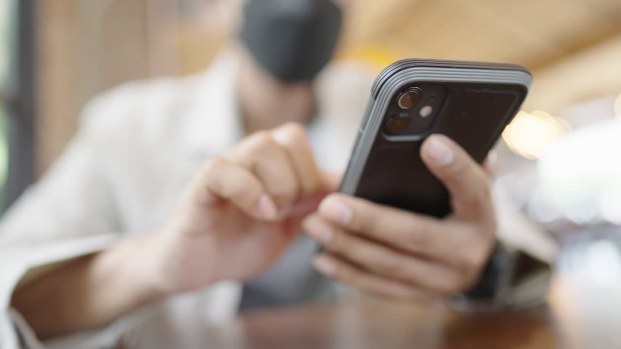 un joven empresario con una máscara quirúrgica está tomando una videoconferencia con los clientes a través de un teléfono inteligente conectado a internet.