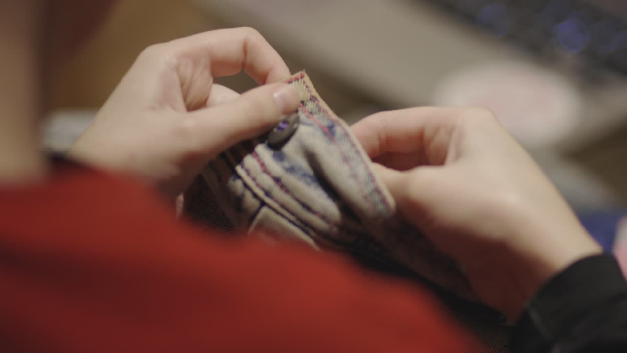 Een vrouw naait een knoop op een vervaagde spijkerbroek.