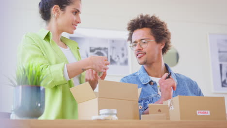 Pareja-Que-Dirige-Negocios-En-Línea-Desde-Casa-Empacando-Y-Etiquetando-Velas-Boutique-Listas-Para-Enviar