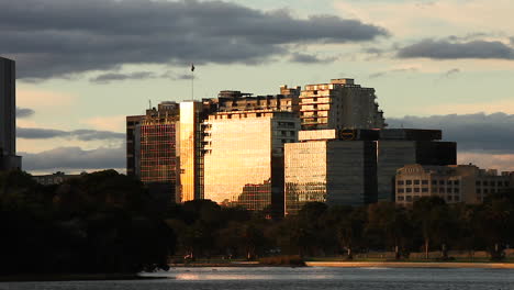 large glass facade reflecting golden light down onto the busy road and park below