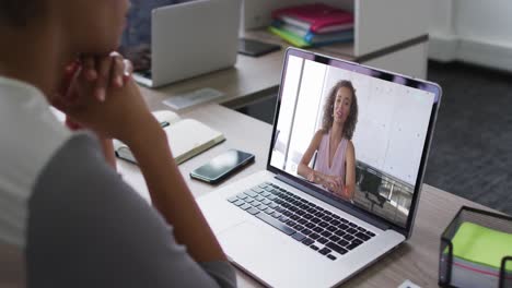 mujer de negocios afroamericana sentada en un escritorio usando una computadora portátil haciendo una videollamada con una colega